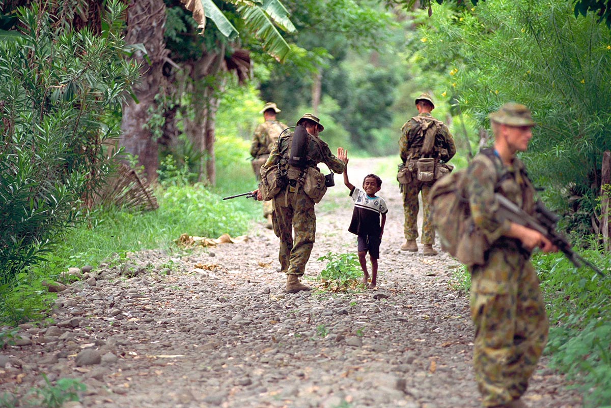 "High five mister".  A local kid greets A Coy 3RAR soldiers on patrol in Oecussi. Patrols were designed as much for visibility and confidence building in the community as they were for security. This photo was later published on the front cover of the official INTERFET book. Photo by Brian Hartigan.