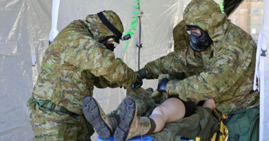 Troops cut a simulated nerve agent casualty out of her contaminated clothing as she passes through the personnel decontamination station. Story and photo by Captain Chris Wade.