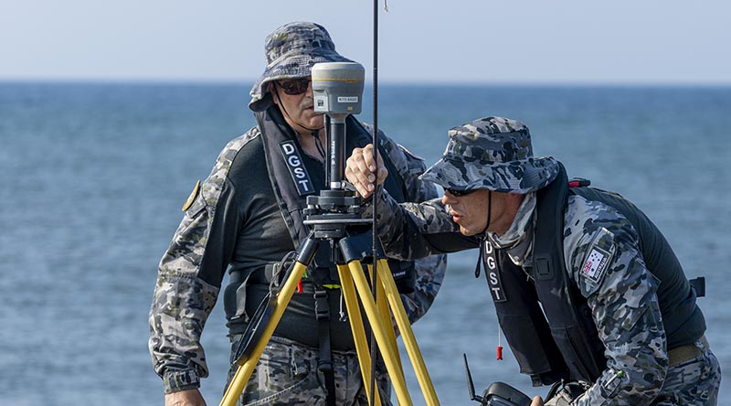 Royal Australian Navy hydrographer Able Seaman Richard Nico (right) and Petty Officer Nicholas Grove set up a tripod-mounted GNSS base station at Banongan beach, Indonesia, during Exercise Keris Woomera 26. Photo by Corporal Jack Pearce.